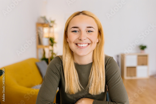 Portrait of young millennial woman looking at camera at home. Close-up screen laptop view of beautiful girl with joyful expression listening on laptop video call. Happiness and people concept