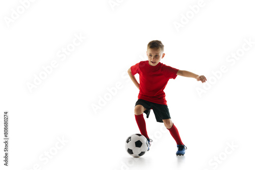 Athletic, sportive boy training dribbling technique in motion against white studio background. Dynamic shot. Concept of professional sport, championship, youth league, hobby. Ad