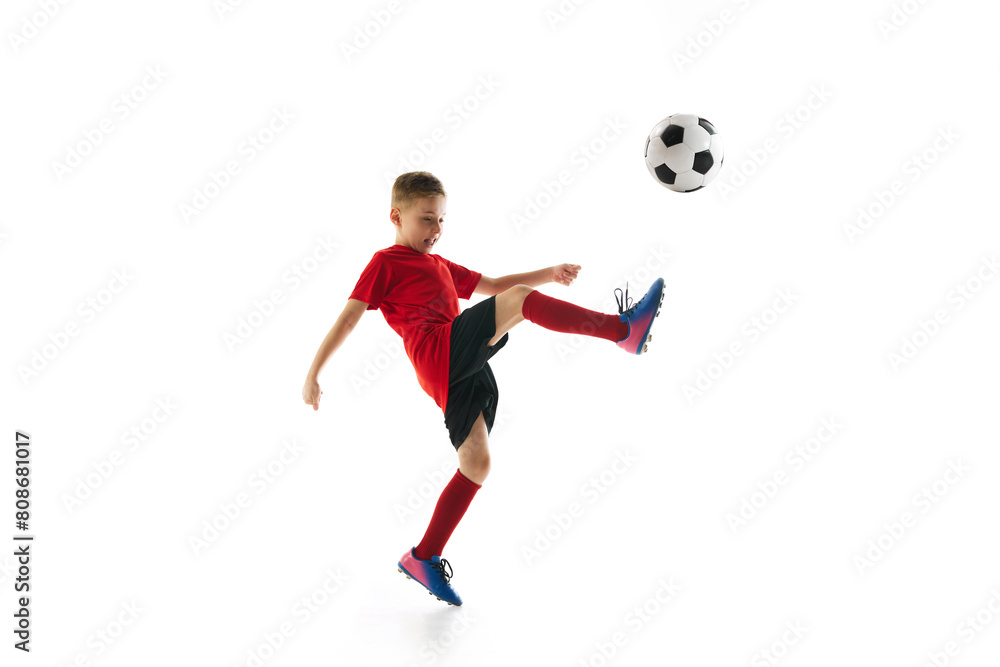 Little sportive boy with soccer ball doing flying kick in motion against white studio background. Dynamic portrait. Concept of professional sport, championship, youth league, hobby. Ad