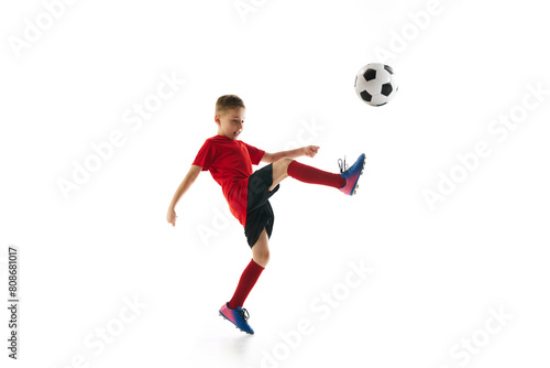 Little sportive boy with soccer ball doing flying kick in motion against white studio background. Dynamic portrait. Concept of professional sport, championship, youth league, hobby. Ad