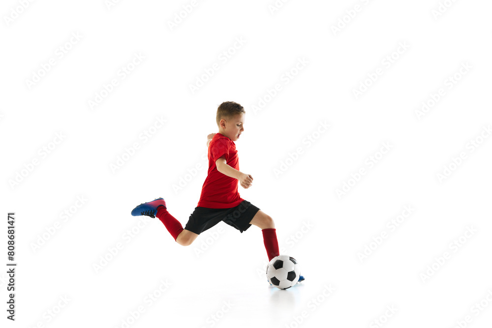 Boy kicking soccer ball in motion to take perfect pass against white studio background. Training exercises. Concept of professional sport, championship, youth league, hobby. Ad