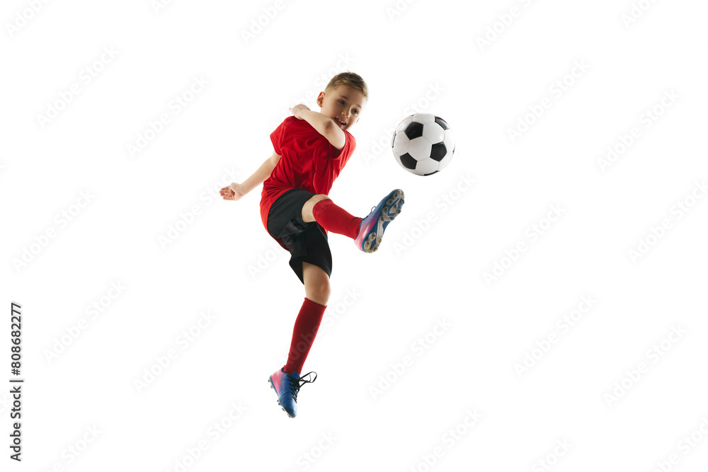 Little sporty boy with soccer ball doing flying kick in motion against white studio background. Concept of professional sport, championship, youth league, hobby. Ad