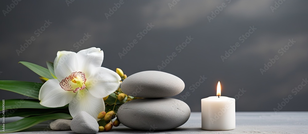 A serene setting with spa stones a burning candle and flowers arranged on a grey background ideal for a copy space image A serene setting with spa stones a burning candle and flowers arranged on a grey background ideal for a copy space image