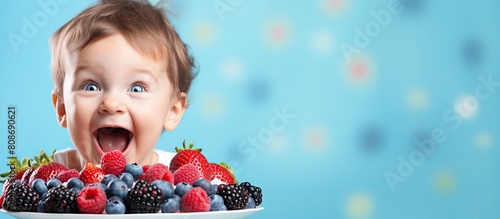 Happy one year old boy celebrating his birthday with a healthy homemade cake topped with berries The vibrant blue background and copy space image capture the child s joyful and surprised emotions dur photo