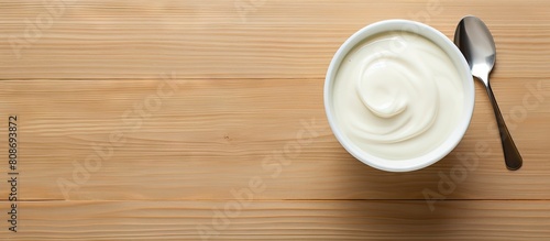 A top down view of a cup and spoon containing fresh and thick sour cream on a table with a blank space nearby for text in the image. Copy space image. Place for adding text and design