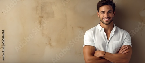 Image of a confident satisfied and cool young man smiling to the camera with crossed arms seen from the side against a flat wall. Copy space image. Place for adding text and design photo