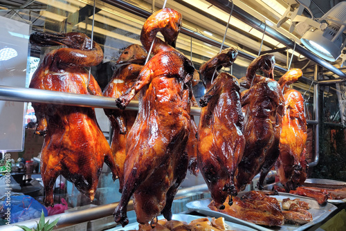 Roasted crispy ducks hanging from metal hooks in the window of a Chinese restaurant.
