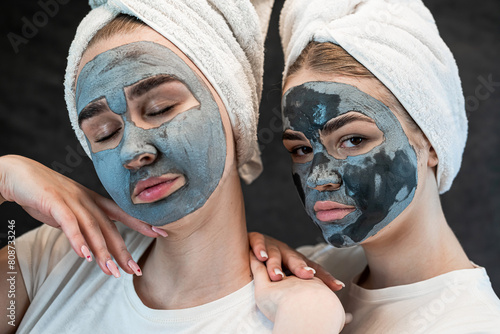 Two sister girls with a mud or clay mask on their faces, enjoy spa treatments isolated on black