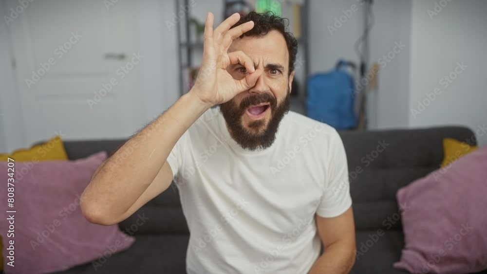 Shocked middle age man at home wearing white t-shirt, expresses surprise with an 'ok' gesture, humor in his eyes as they look through his fingers! Shocked middle age man at home wearing white t-shirt, expresses surprise with an 'ok' gesture, humor in his eyes as they look through his fingers!