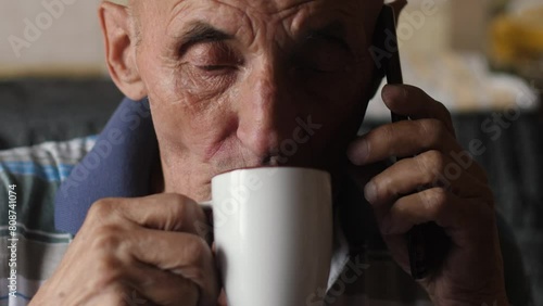 Caucasian pensioner 70 -79 years old drinking coffee from a cup and talking on the phone while inside. an elderly man has breakfast with tea and discusses problems photo
