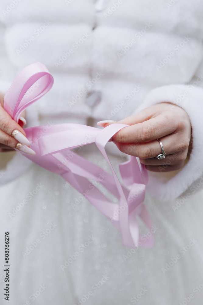a bride in a white wedding dress and a white fur coat holds pink ribbons in her hands a bride in a white wedding dress and a white fur coat holds pink ribbons in her hands