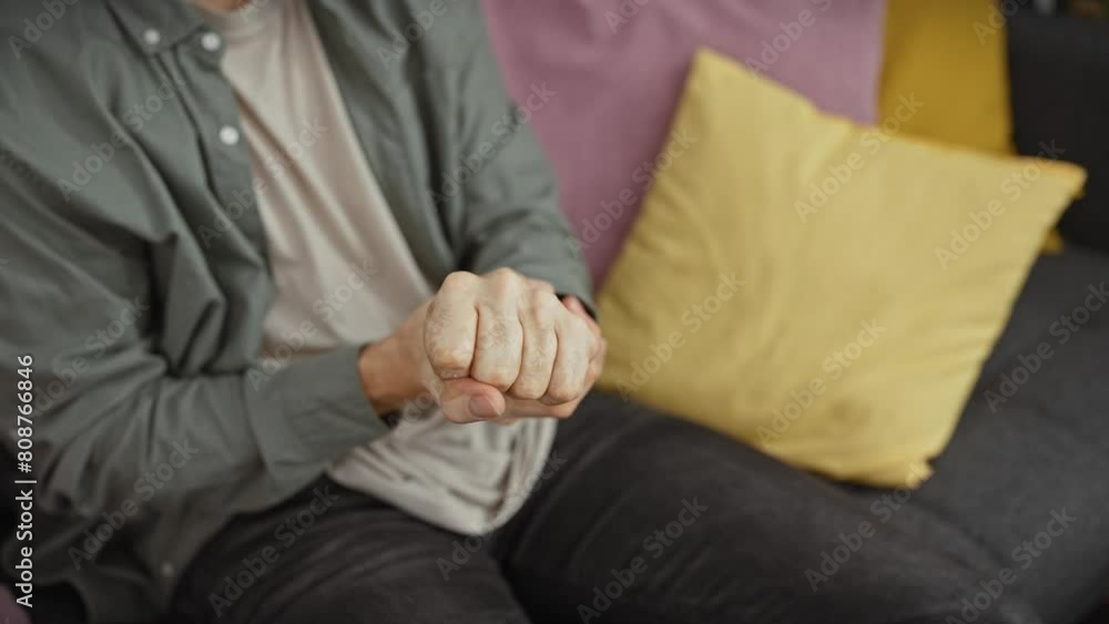 Young hispanic man with beard at home shows wrist pain while sitting on couch, indoor setting Young hispanic man with beard at home shows wrist pain while sitting on couch, indoor setting