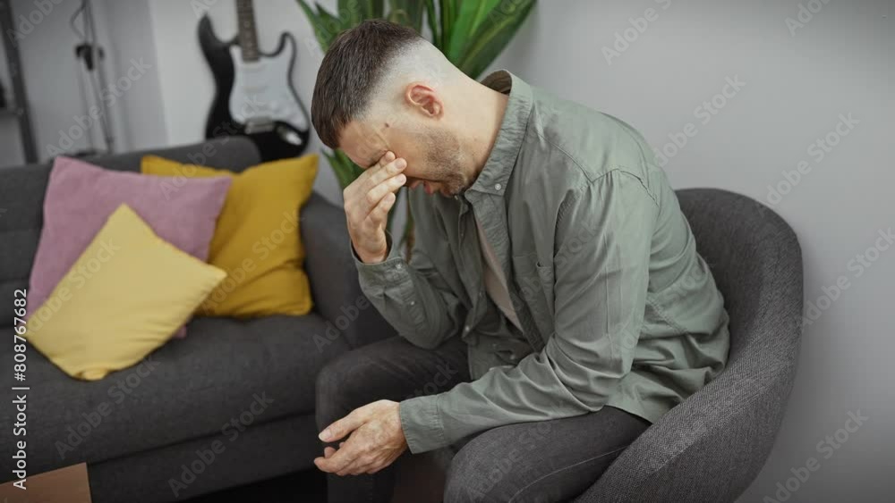A distressed man sits in an apartment room, looking tired and worried. A distressed man sits in an apartment room, looking tired and worried.