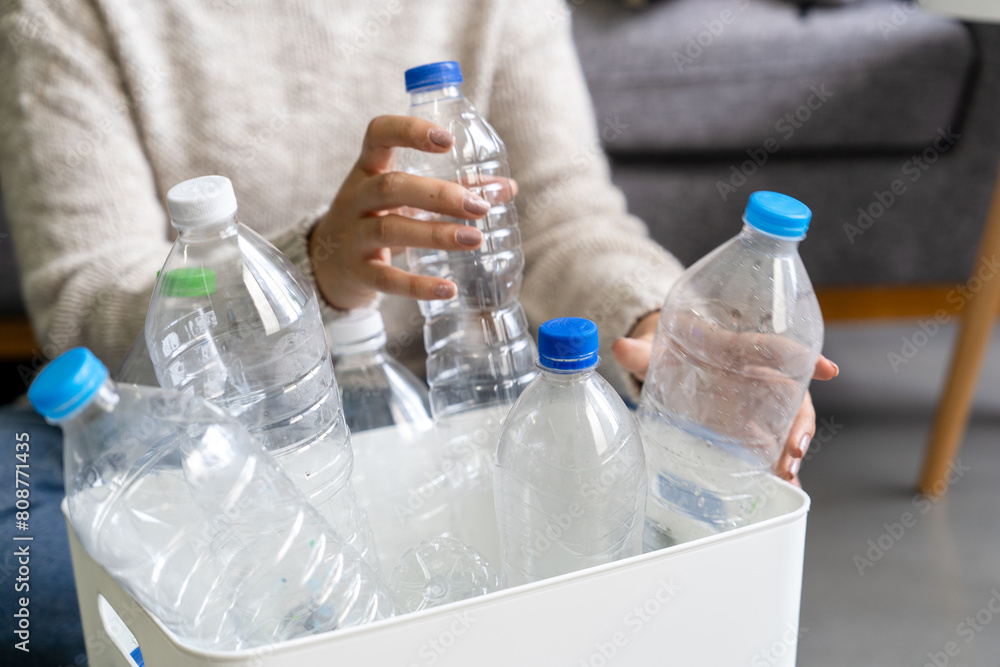A woman wearing a cream sweater collects and sorts recycled plastic bottles into white trash cans. A woman wearing a cream sweater collects and sorts recycled plastic bottles into white trash cans.