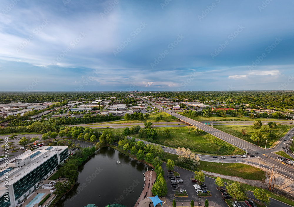 A distant aerial view of downtown Lexington, KY, from the intersection of New Circle Road and Nicholasville Road, showcases the pond of the Lexington Green shopping and entertainment complex