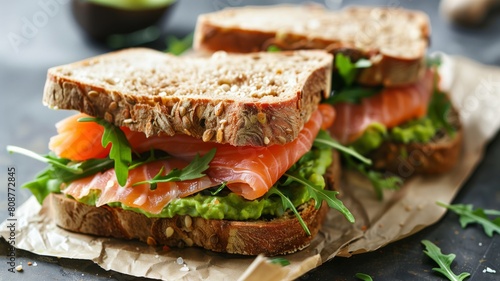 A mouthwatering wheat bread sandwich with salmon, arugula, and gourmet ingredients showcased on a piece of paper