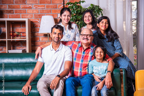 Happy Indian asian family consists of grandparents, parents and kids posing for photo sitting on sofa photo