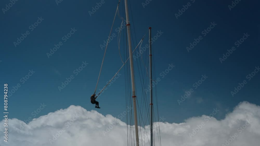 An extreme athlete swings on a rope and performs a somersault in the air. A tourist attraction is a slingshot or catapult. The concept of brave and courageous personalities. High in the mountains abov An extreme athlete swings on a rope and performs a somersault in the air. A tourist attraction is a slingshot or catapult. The concept of brave and courageous personalities. High in the mountains abov