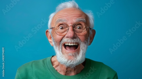 Cheerful elderly man with white beard and glasses laughs happily against blue background photo