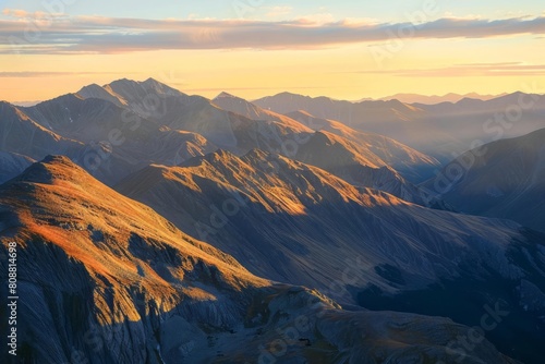 A mountain range at sunrise, with the peaks illuminated in gold against the shadowed valleys
