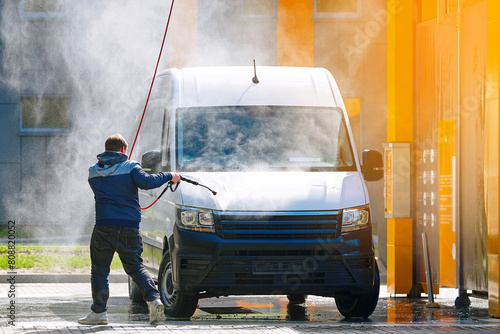 Man using spray nozzle at  self-service car wash to clean van, process of washing   ehicle with water spray. Self-service car wash station with man washing van. Man washes car at contactless car wash