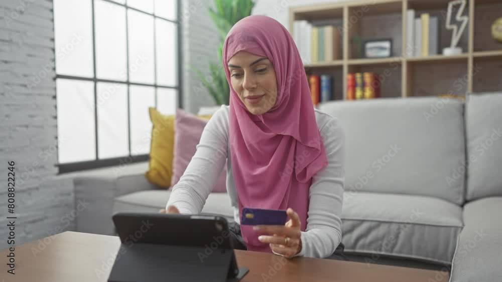 Smiling woman in hijab using credit card and tablet for online shopping in cozy living room. Smiling woman in hijab using credit card and tablet for online shopping in cozy living room.