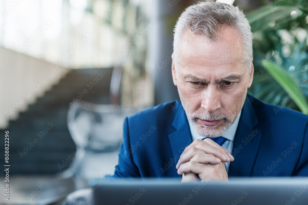Fototapeta premium Senior businessman boss CEO investor lawyer working on laptop computer while sitting at lobby modern office, analyzes market information statistics. Thoughtful man looking on screen