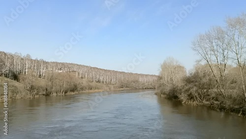 Tall bare trees at a bend in the bed of a calm small river flowing through a hilly valley on a clear spring evening. Inya River, Novosibirsk, Siberia, Russia. photo