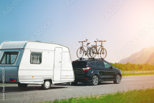 Black suv with bicycles mounted on top tows a white caravan on a road trip with scenic mountains in the background