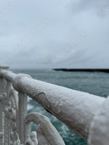 Rain-covered white wrought iron hand rail. Gray skies and stormy seas in the background. © Travis