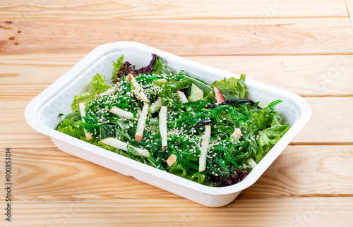 Hakkaido salad with chuka seaweed, juicy apple and nut sauce. Healthy food. Takeaway food. On a wooden background.