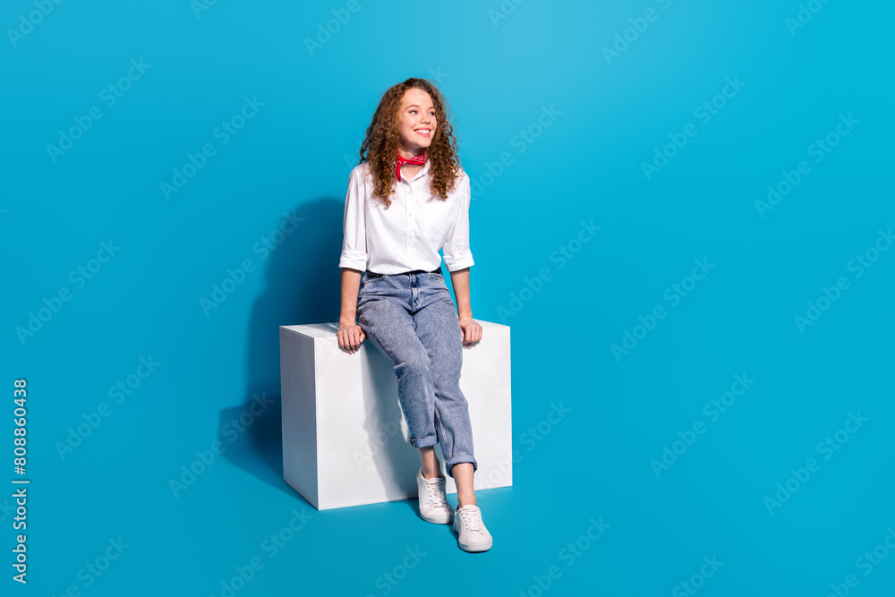 Photo portrait of nice young lady sit cube look empty space wear trendy white garment isolated on blue color background Photo portrait of nice young lady sit cube look empty space wear trendy white garment isolated on blue color background