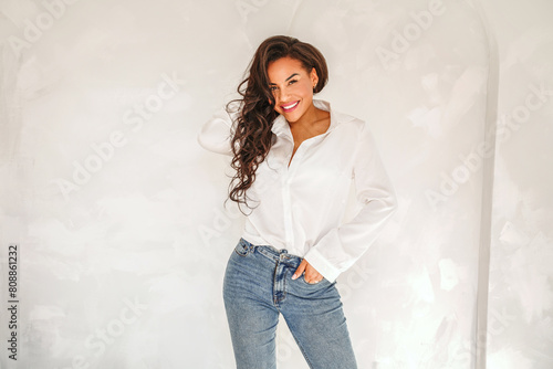 Beautiful woman posing in white shirt and jeans, casual elegant look. Smiling attractive lady with long dark hair looking at the camera.