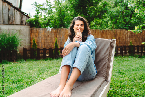One young caucasian woman is relaxing on easy bed while drinking cold coffee in her backyard 