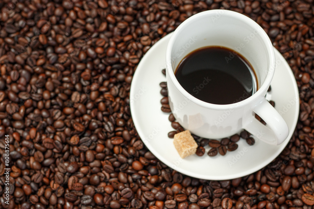 Black coffee in a white cup with a sugar cube on a background of coffee beans. Black coffee in a white cup with a sugar cube on a background of coffee beans.