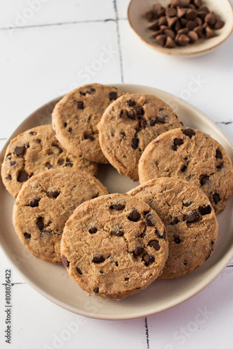 Plate of chocolate chip cookies with extra chocolate chips on side  set on a tiled background