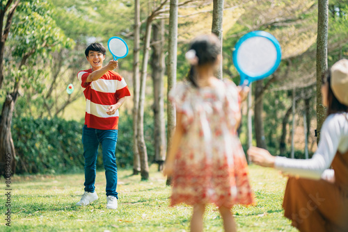 An Asian family of three heads to the park for a picnic, indulging in games and blowing bubbles together. 