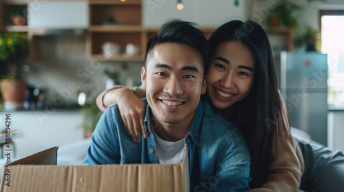Portrait of young attractive happy asian couple man sitting at new home smiling to camera with carton package box storage to move in empty house. LGBTQ relationship and relocating concept Stock Photo  photo