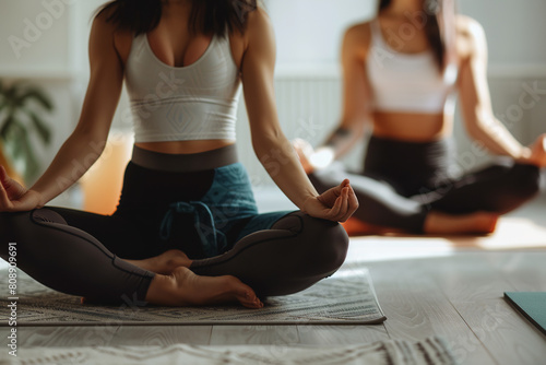 Close up of two women doing yoga in the gym. One woman is wearing leggings and has her hands on her knees while sitting down