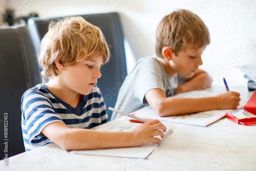 Two boys doing homework together. Brothers, siblings and twins learning at home. Elementary school students, children writing.
