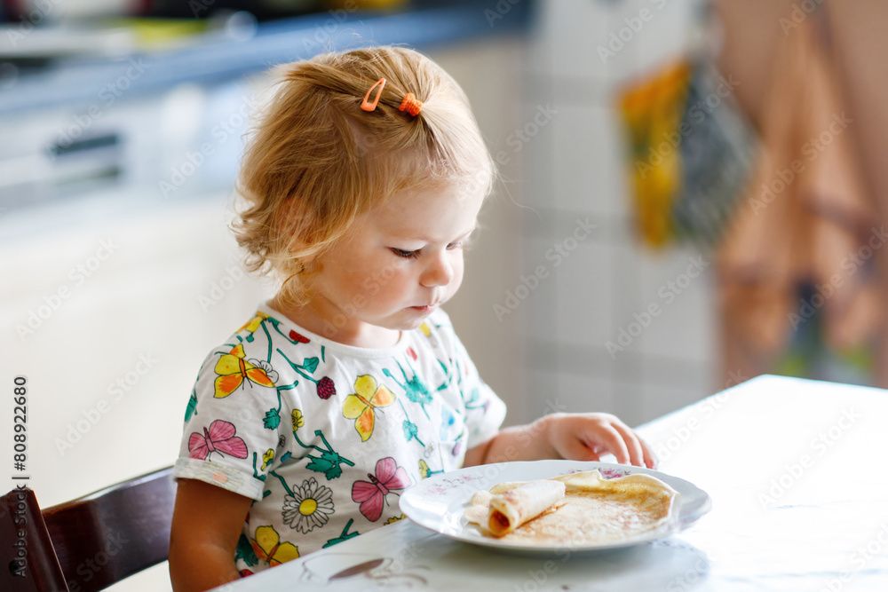 Happy little toddler girl eating delicious pancakes sitting in the kitchen. Cute child tasting different food Happy little toddler girl eating delicious pancakes sitting in the kitchen. Cute child tasting different food