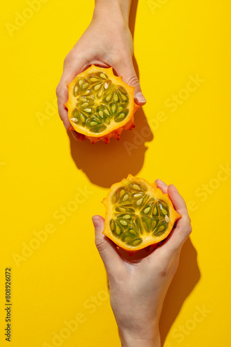 Two half of kiwano fruit in hands on yellow background  top view