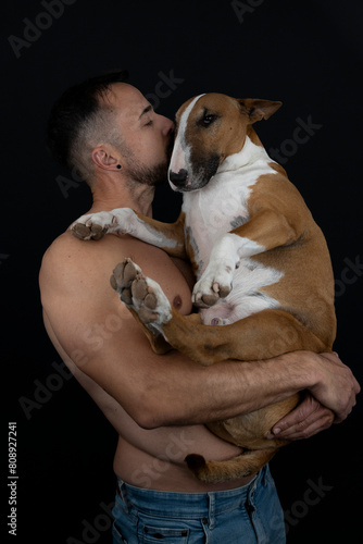 Strong shirtless man on black background kissing his dog