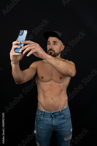 Strong shirtless man on black background wearing cap taking selfie