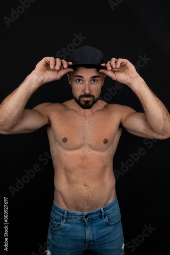Strong shirtless man on black background touching his cap