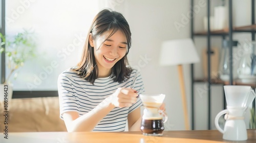 Young woman making coffee at home. She is smiling and looks happy. The photo is taken from a side angle. photo