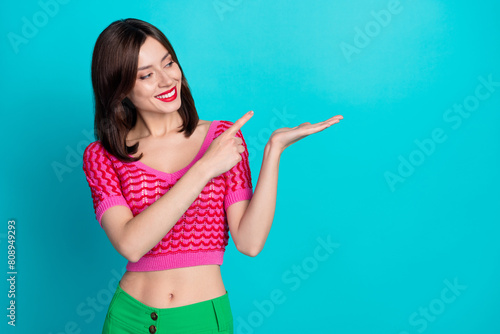 Portrait of cheerful pretty lovely girl wear pink top look indicating at product on hand empty space isolated on blue color background photo