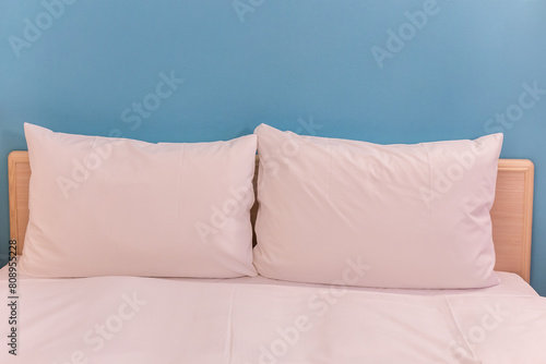 White pillows on a wooden bed with a blue wall as a background.