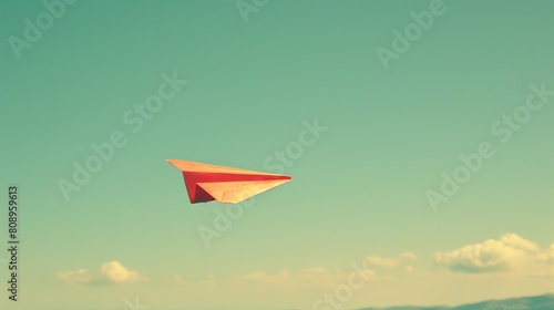 A single paper airplane flying against a clear sky.