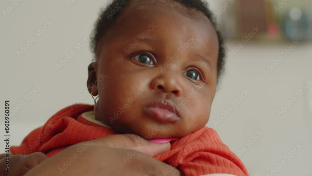 Close up of adorable black baby girl in orange clothes in loving mothers hands Close up of adorable black baby girl in orange clothes in loving mothers hands